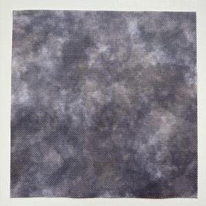 May include: A square piece of fabric featuring a mottled, tie-dye style pattern in shades of dark charcoal gray, slate, and soft white. The material has a visible, uniform woven grid texture throughout the entire surface area.