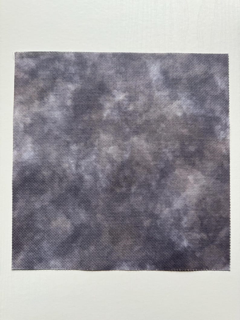 May include: A square piece of fabric featuring a mottled, tie-dye style pattern in shades of dark charcoal gray, slate, and soft white. The material has a visible, uniform woven grid texture throughout the entire surface area.