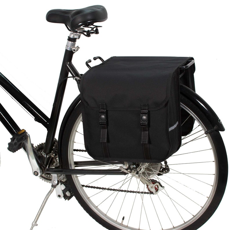 May include: Black bicycle with a black rear rack and two black panniers. The bicycle has a black seat and a black kickstand.