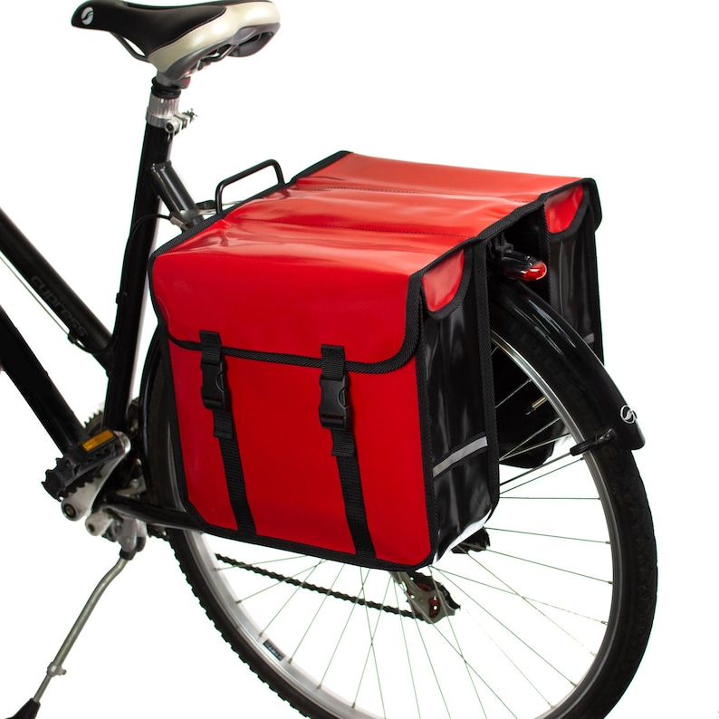 May include: A red and black bicycle pannier bag with reflective accents attached to a black bicycle.
