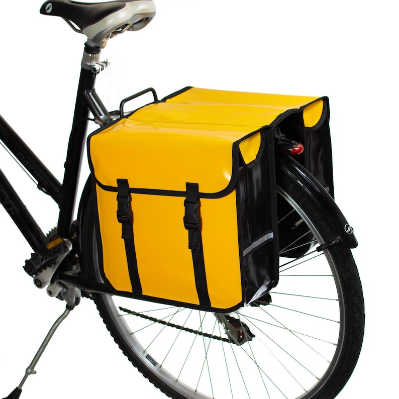 May include: A yellow and black bicycle pannier bag with reflective accents. The bag is attached to the rear rack of a bicycle.