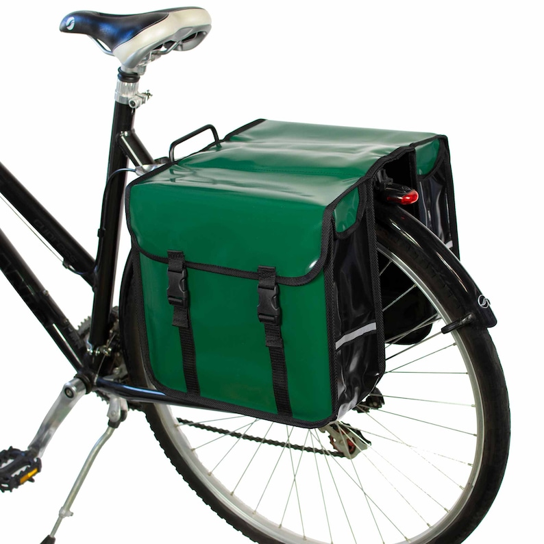 May include: A green and black bicycle pannier bag with a reflective strip. The bag is attached to the rear rack of a bicycle.