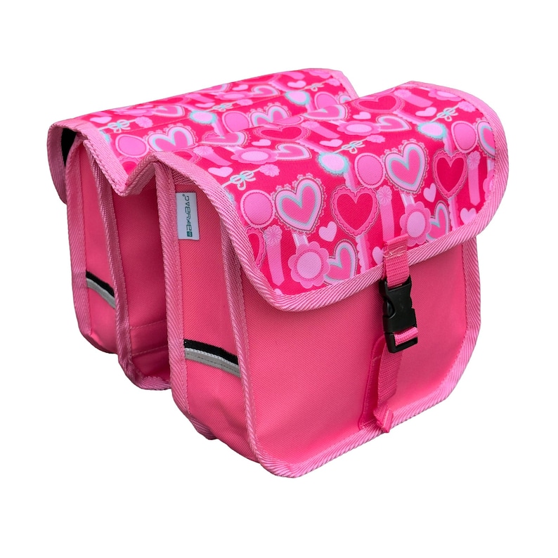 May include: A pair of bright pink bicycle pannier bags featuring a repeating pattern of hearts and circular floral motifs on the top flaps. Each bag has a black plastic buckle closure, pink fabric trim, and a small reflective strip on the side.