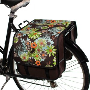 Pu&ograve; includere: Una borsa da bicicletta marrone con una stampa floreale con fiori verdi, blu e arancioni. La borsa &egrave; attaccata a una bicicletta nera.
