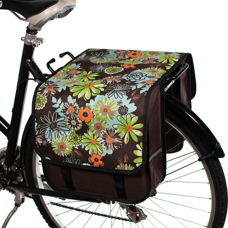 Pu&ograve; includere: Una borsa da bicicletta marrone con una stampa floreale con fiori verdi, blu e arancioni. La borsa &egrave; attaccata a una bicicletta nera.