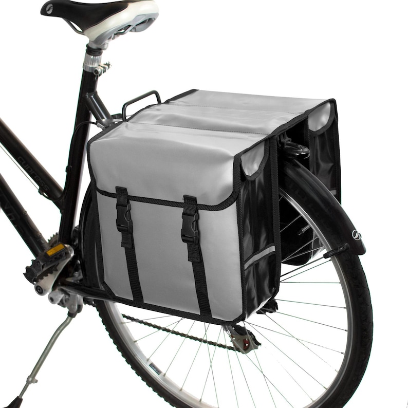 May include: A pair of gray and black bicycle panniers with reflective accents attached to a black bicycle.