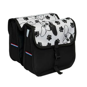 May include: A black double bicycle pannier bag featuring a white flap with a repeating pattern of black and white dog faces and paw prints. The bag includes a black plastic buckle closure and a small blue, white, and red striped fabric tag.