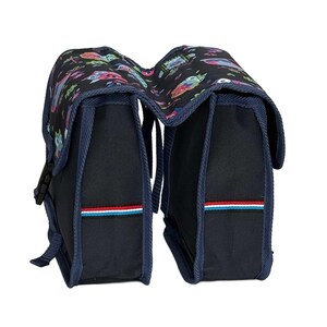 May include: A black double bicycle pannier bag featuring a colourful owl pattern on the top flaps. The bag has dark blue trim, side buckles, and a horizontal stripe detail in red, white, and light blue on the front of each compartment.