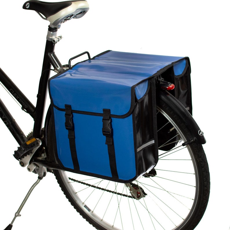 May include: A blue and black bicycle pannier set with two large compartments and adjustable straps. The panniers are attached to the rear rack of a bicycle.