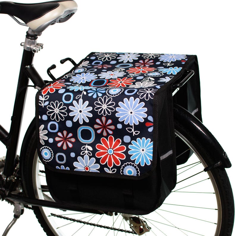 Pu&ograve; includere: Una borsa da bicicletta nera con una stampa floreale con fiori rossi, blu e bianchi su uno sfondo blu scuro. La borsa &egrave; attaccata a una bicicletta nera.