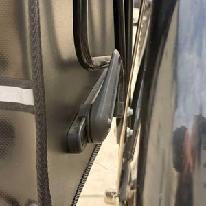 May include: Close-up of a black bicycle pannier bag attached to a bike rack. The bag has a reflective stripe and a black locking mechanism. The bike's black mudguard and wheel are also visible.