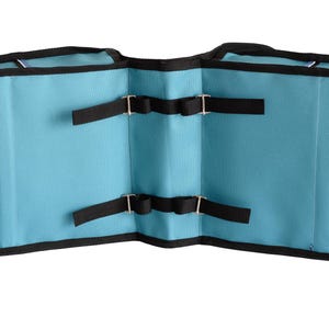 May include: A light blue double-sided saddlebag with black trim and black nylon straps featuring metal buckles. The bag has two main compartments connected by a central bridge, with black hook-and-loop fasteners on the outer edges.