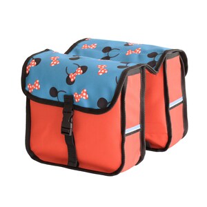 May include: A double bicycle pannier bag featuring a bright red main body with black trim and a blue flap decorated with a repeating pattern of black mouse ears and red polka-dot bows. The bag includes a black plastic buckle closure on the front.