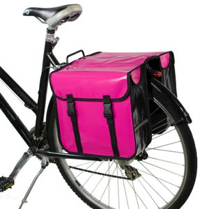 May include: A pink bicycle pannier with black straps and a black reflective strip. The pannier is attached to the rear rack of a black bicycle.