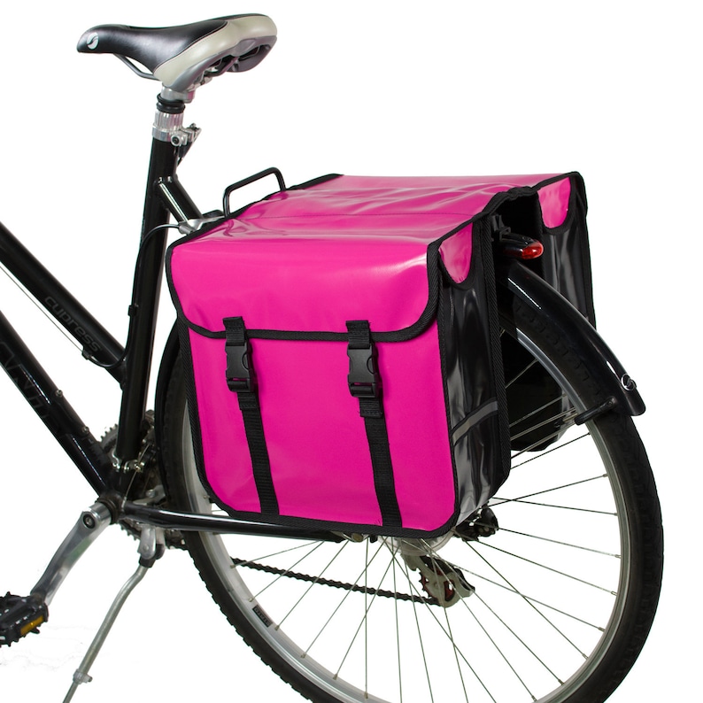 May include: A pink bicycle pannier with black straps and a black reflective strip. The pannier is attached to the rear rack of a black bicycle.