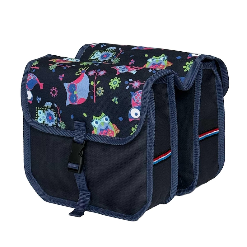 May include: A double bicycle pannier bag in dark navy blue featuring a colourful owl and floral pattern on the top flaps. The bag includes adjustable black plastic buckle closures, reinforced blue fabric trim, and small red, white, and blue accents.