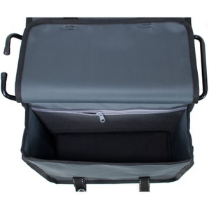 May include: A black and grey bike rack bag with a zipped pocket and two straps. The bag is open and the inside is visible.