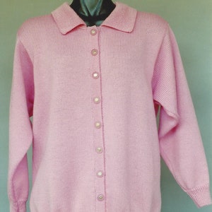 May include: A pink knitted cardigan with a collared neckline and a button-up front. The cardigan has long sleeves and a ribbed texture.
