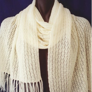 May include: A white crocheted scarf with a fringe on the ends. The scarf is draped over a mannequin.