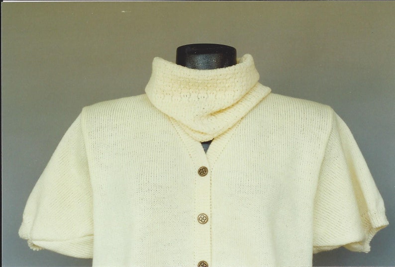 May include: A white knitted sweater with a high collar and short sleeves. The sweater has a button-up front and is made of a soft, lightweight material.