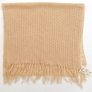 May include: A beige knitted scarf with a fringe border. The scarf is made of a lightweight, open weave fabric. The tag on the scarf reads "Hand Woven Scarf".