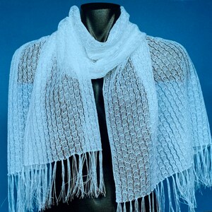 May include: White crocheted scarf with fringe. The scarf is made of a delicate, openwork pattern.