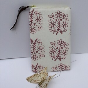 May include: A white zippered pouch with a floral print in shades of pink and brown. The pouch has a brown fabric zipper pull.