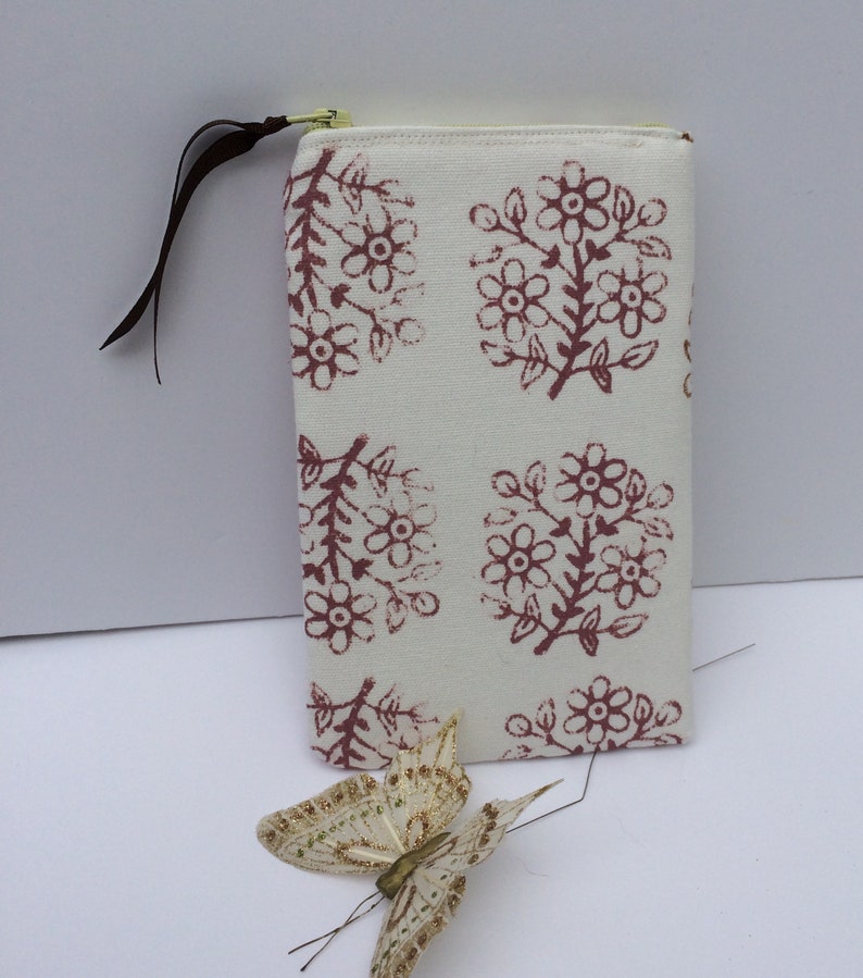 May include: A white zippered pouch with a floral print in shades of pink and brown. The pouch has a brown fabric zipper pull.