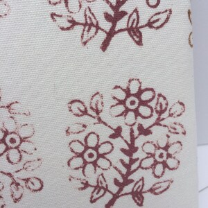 May include: Close-up of a white fabric with a repeating pattern of brown floral designs. The fabric has a subtle texture.