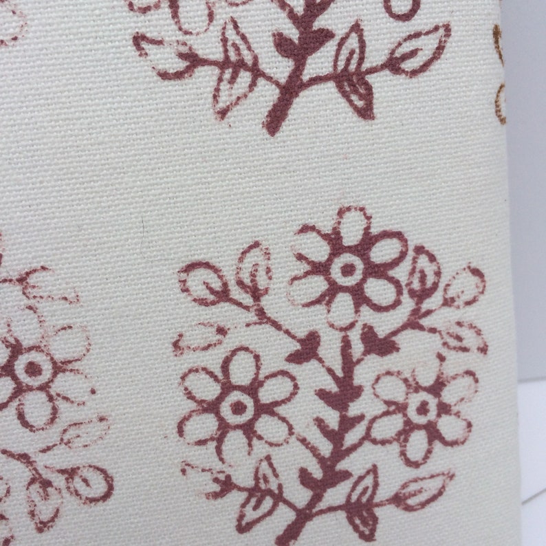 May include: Close-up of a white fabric with a repeating pattern of brown floral designs. The fabric has a subtle texture.