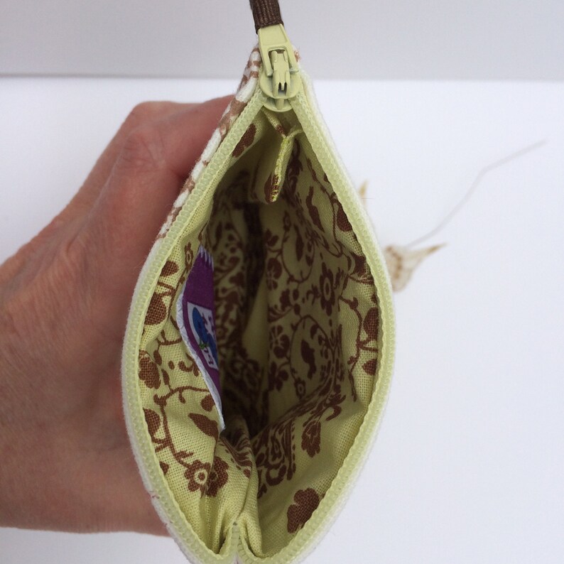 May include: A small, zippered pouch with a green and white floral pattern. The inside of the pouch is lined with a light green fabric with a brown floral pattern.