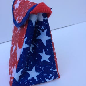 Puede incluir: Una bolsa de almuerzo roja, blanca y azul con un patr&oacute;n de estrellas. La bolsa est&aacute; hecha de un tejido duradero y tiene un cierre de cremallera.