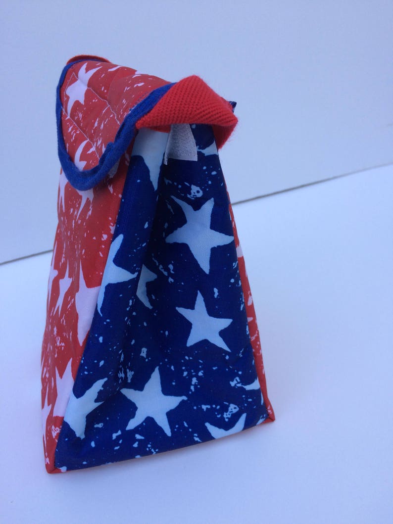 Puede incluir: Una bolsa de almuerzo roja, blanca y azul con un patr&oacute;n de estrellas. La bolsa est&aacute; hecha de un tejido duradero y tiene un cierre de cremallera.