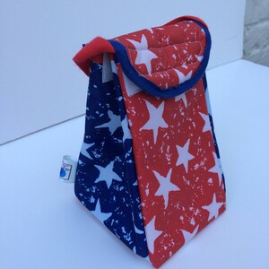 Puede incluir: Una bolsa de almuerzo roja y azul con un patr&oacute;n de estrellas blancas. La bolsa tiene un ribete azul y un asa.