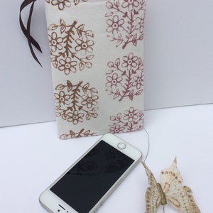 May include: A white zippered pouch with a floral print in shades of brown and pink. The pouch is lying on a white surface next to a black smartphone and a white butterfly.