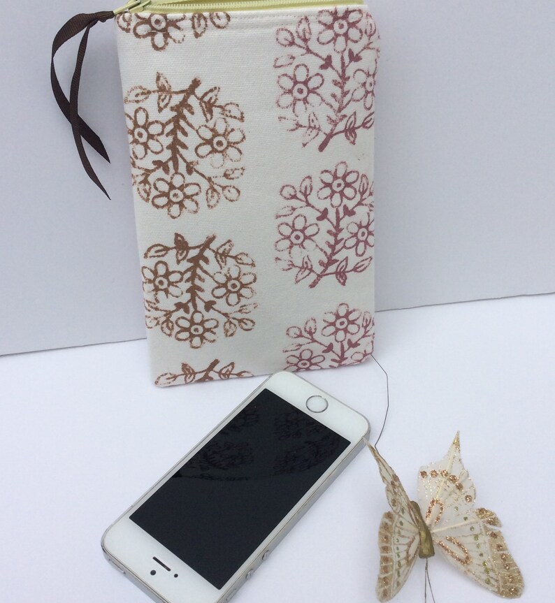 May include: A white zippered pouch with a floral print in shades of brown and pink. The pouch is lying on a white surface next to a black smartphone and a white butterfly.