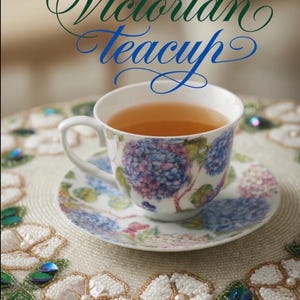 May include: A Victorian teacup filled with tea, resting on a matching saucer. The teacup and saucer are decorated with blue and purple floral patterns. The text "Victorian Teacup" is written above the teacup in green and blue script.