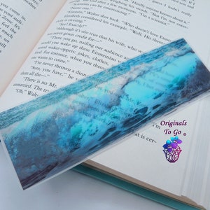 May include: A blue and green abstract watercolor bookmark with the text "Originals To Go" in white. The bookmark features a wave-like design with a white, foamy crest.