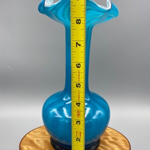 Puede incluir: Un jarr&oacute;n de vidrio azul con una abertura ancha y acampanada y un cuello estrecho. El jarr&oacute;n mide aproximadamente 23 cm de alto.