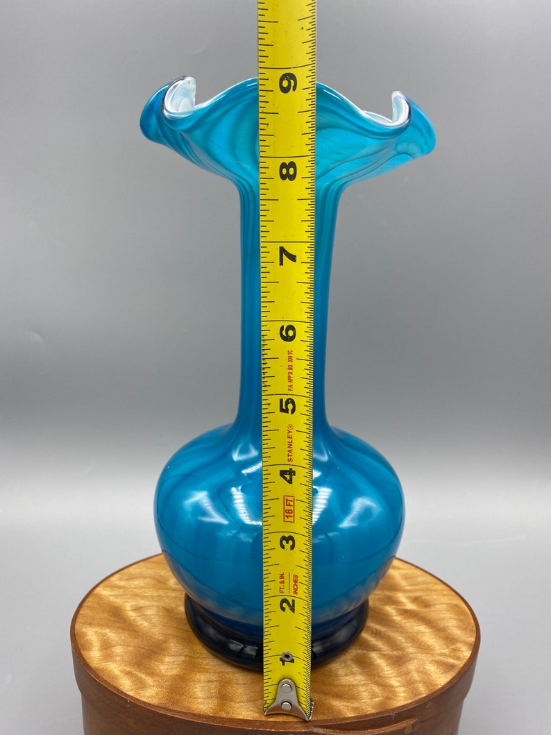 Puede incluir: Un jarr&oacute;n de vidrio azul con una abertura ancha y acampanada y un cuello estrecho. El jarr&oacute;n mide aproximadamente 23 cm de alto.