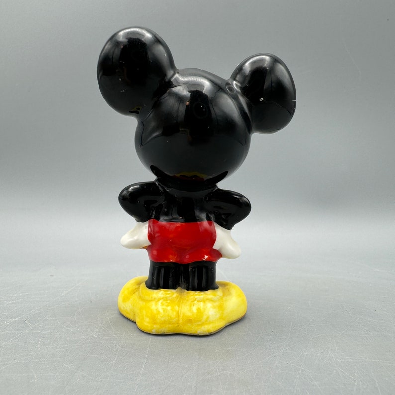 Może przedstawiać: Ceramiczna figurka Myszki Miki w kolorze czarnym i czerwonym. Miki stoi z założonymi rękami i ma na sobie swoje charakterystyczne czerwone spodenki i ż&oacute;łte buty.