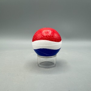 May include: A red, white, and blue ball with a textured surface. The ball is on a clear plastic stand.