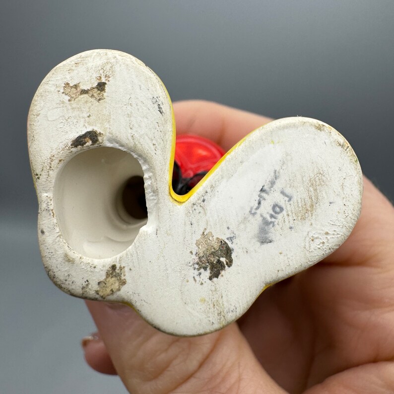 Może przedstawiać: Sp&oacute;d ceramicznej figurki z ż&oacute;łto-czerwonym wzorem. Figurka ma otw&oacute;r na dole do włożenia świeczki. Sp&oacute;d figurki jest oznaczony tekstem "101".