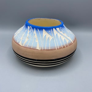 Peut inclure: Un bol en céramique peint à la main avec un motif bleu, blanc et marron. Le bol a un bord large et une base arrondie.