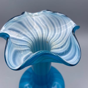 Puede incluir: Un jarr&oacute;n de vidrio azul con un dise&ntilde;o de espiral blanco. El jarr&oacute;n tiene una abertura ancha y acampanada y un cuello estrecho.