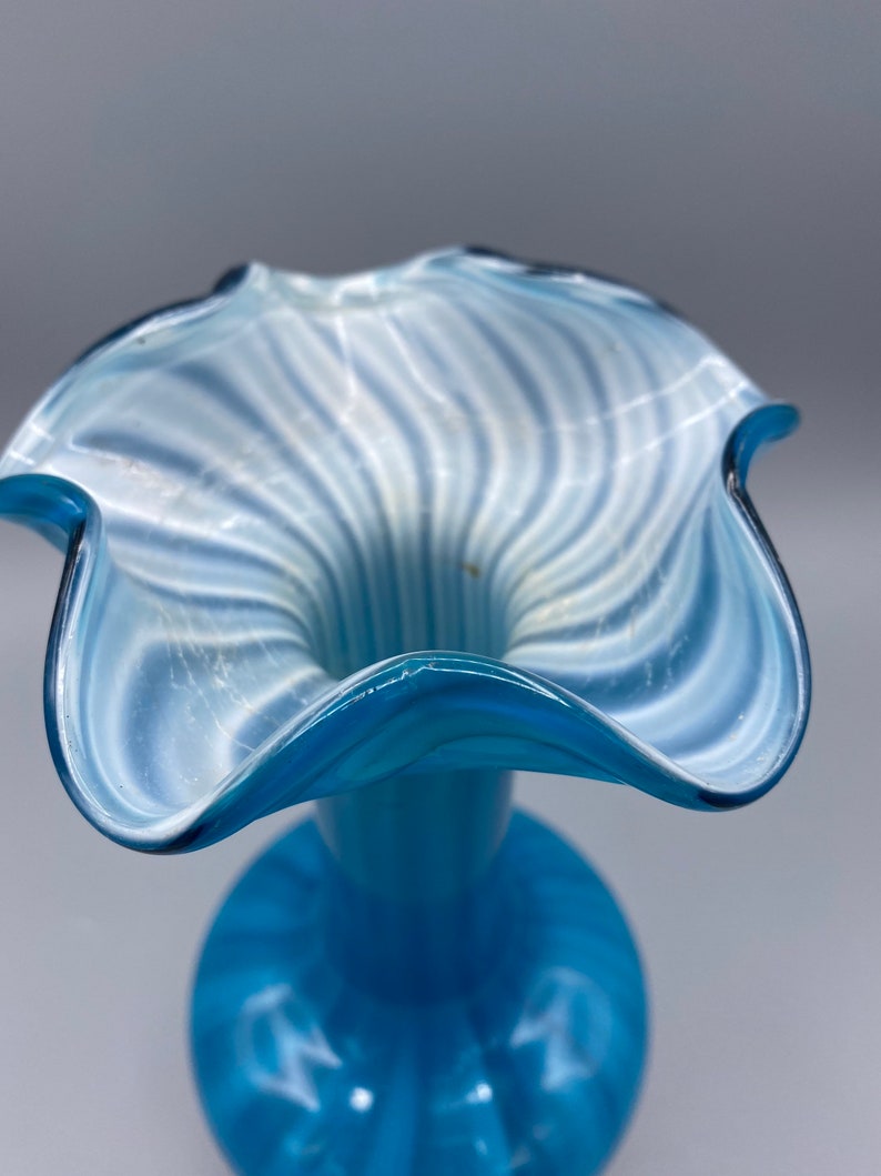Puede incluir: Un jarr&oacute;n de vidrio azul con un dise&ntilde;o de espiral blanco. El jarr&oacute;n tiene una abertura ancha y acampanada y un cuello estrecho.