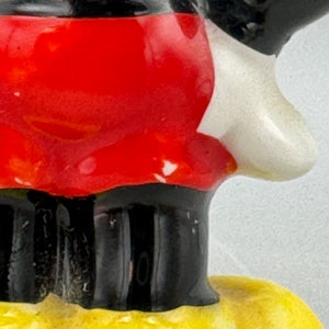 Może przedstawiać: Ceramiczna figurka Myszki Miki w charakterystycznych czerwonych spodenkach, czarnych butach i białych rękawiczkach. Figurka stoi na ż&oacute;łtej podstawie.