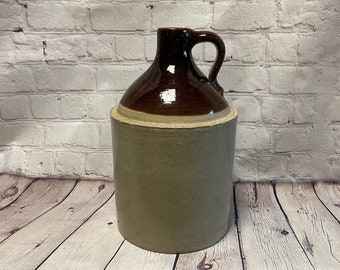 May include: A brown and beige ceramic jug with a handle. The jug has a brown glaze on the top half and a beige glaze on the bottom half.