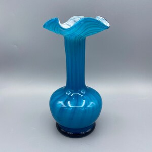 Puede incluir: Un jarr&oacute;n de vidrio azul con una parte superior ondulada y rizada y un patr&oacute;n de espiral. El jarr&oacute;n tiene una base azul oscuro.