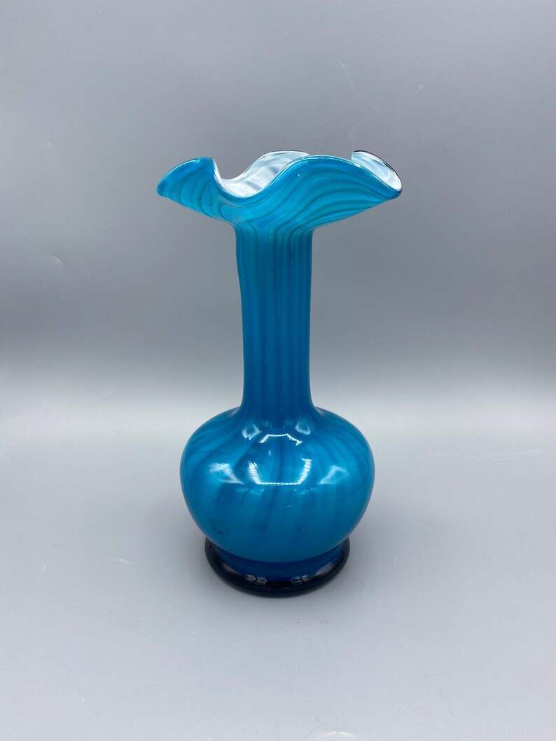 Puede incluir: Un jarr&oacute;n de vidrio azul con una parte superior ondulada y rizada y un patr&oacute;n de espiral. El jarr&oacute;n tiene una base azul oscuro.